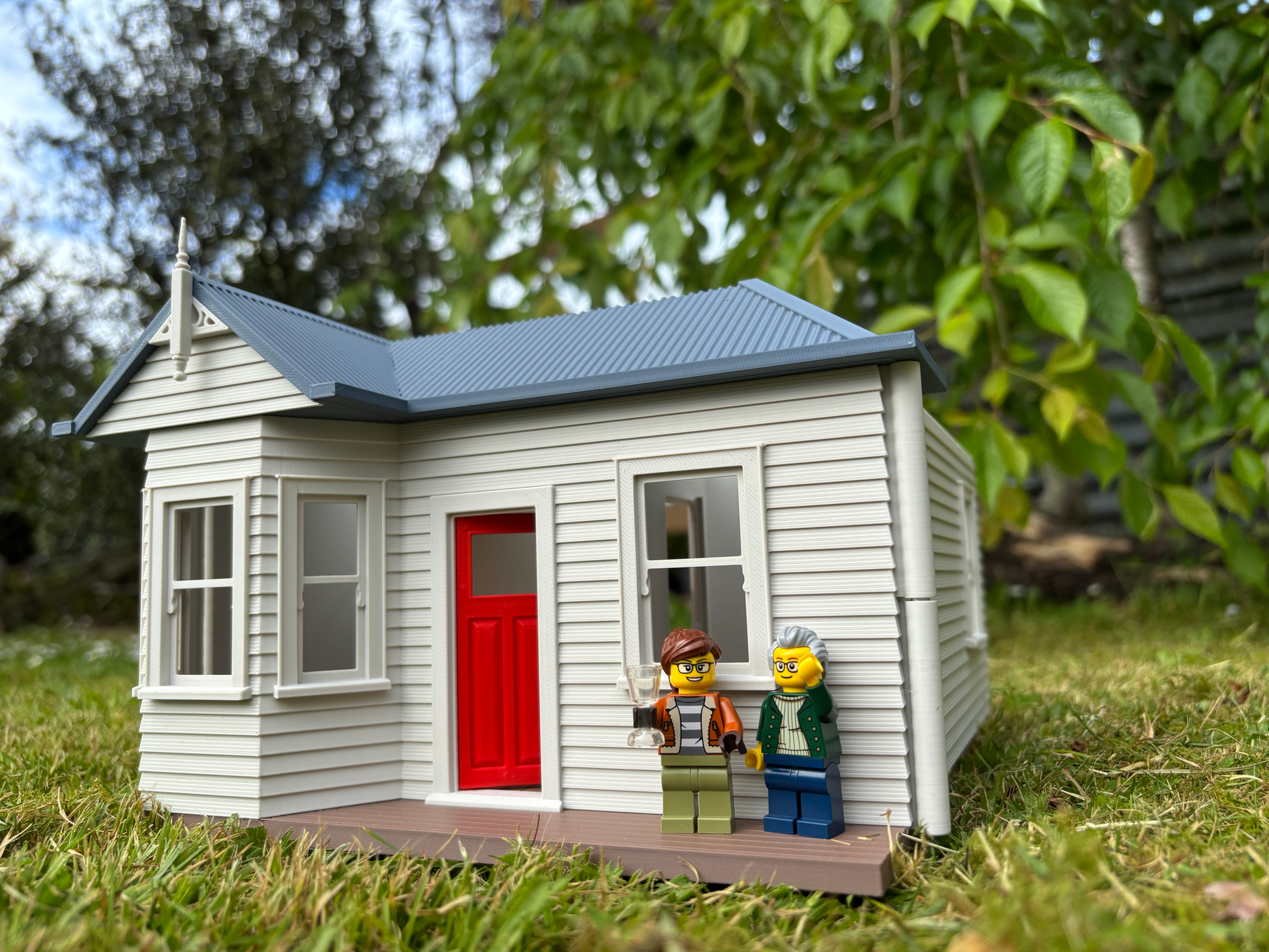 Model of a small house with two LEGO figures standing outside on grass