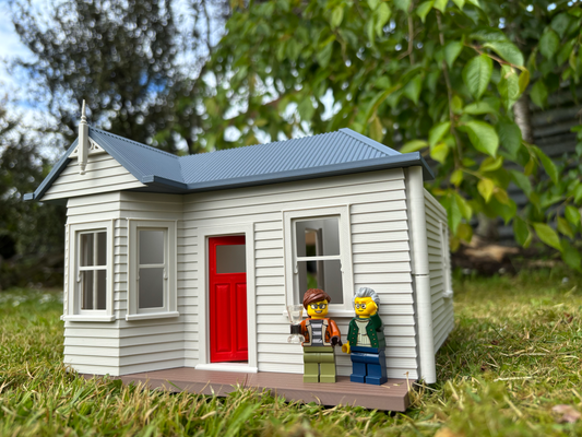 Model of a small house with two LEGO figures standing outside on grass